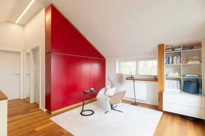 Umgesetzter Wohnraum mit rotem Einbauschrank unter der Dachschräge und hellem Sessel