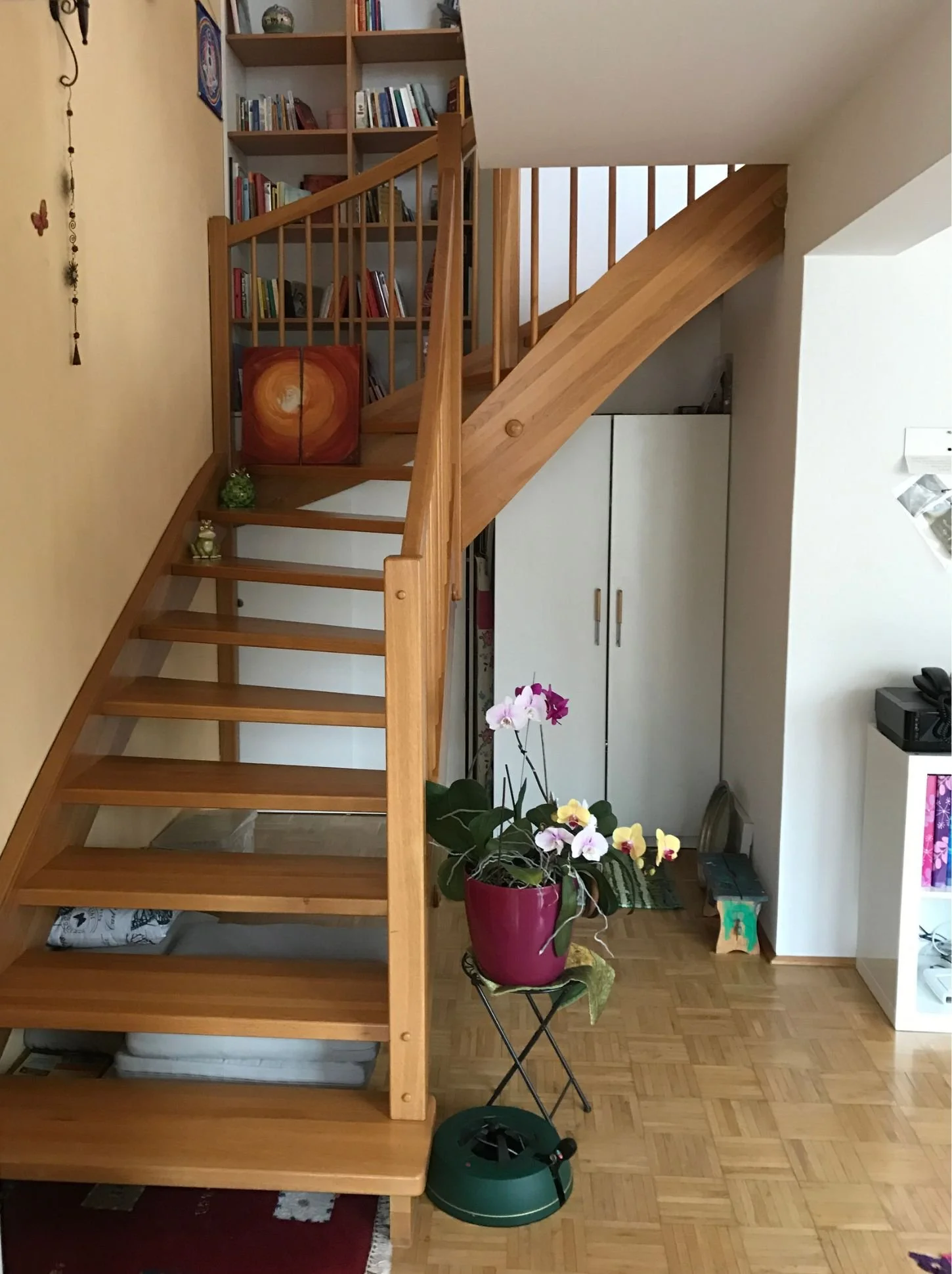 Vorher-Bild eines Wohnbereichs mit offener Holztreppe, Bücherregal und Flur im Bestandszustand – klassische Ausgangssituation vor Renovierung, Modernisierung oder gestalterischer Neugestaltung