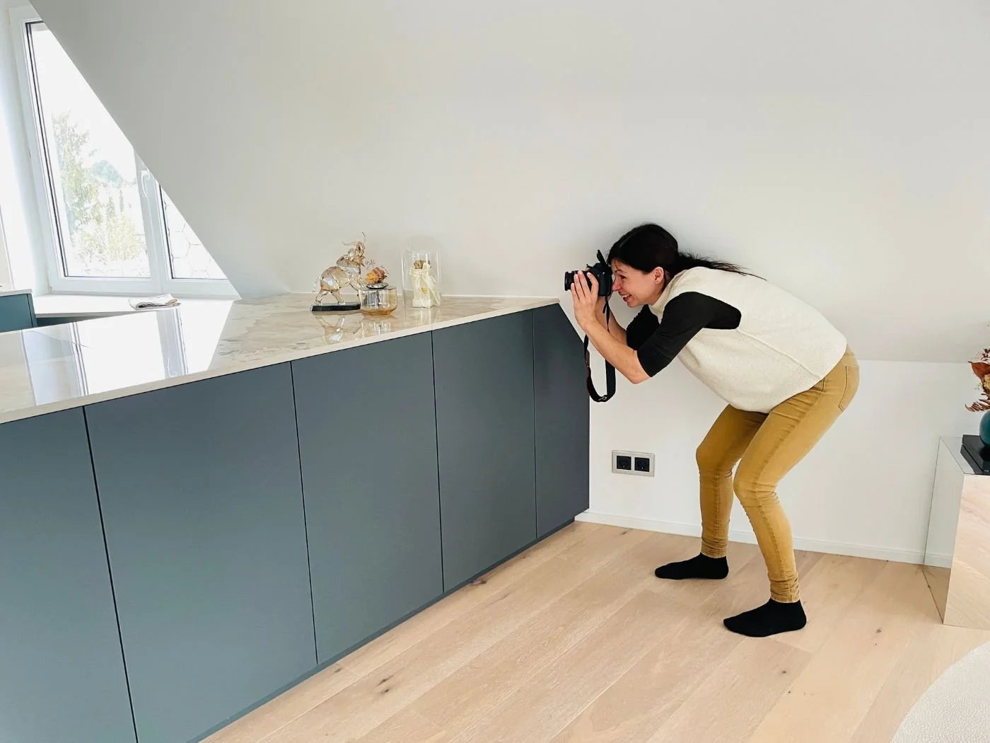 Fotografin fotografiert eine moderne Designküche unter der Dachschräge mit dunklen Fronten und heller Stein-Arbeitsplatte - Küchenplanung, Küchenumbau und Küchenberatung in Wien und Umgebung