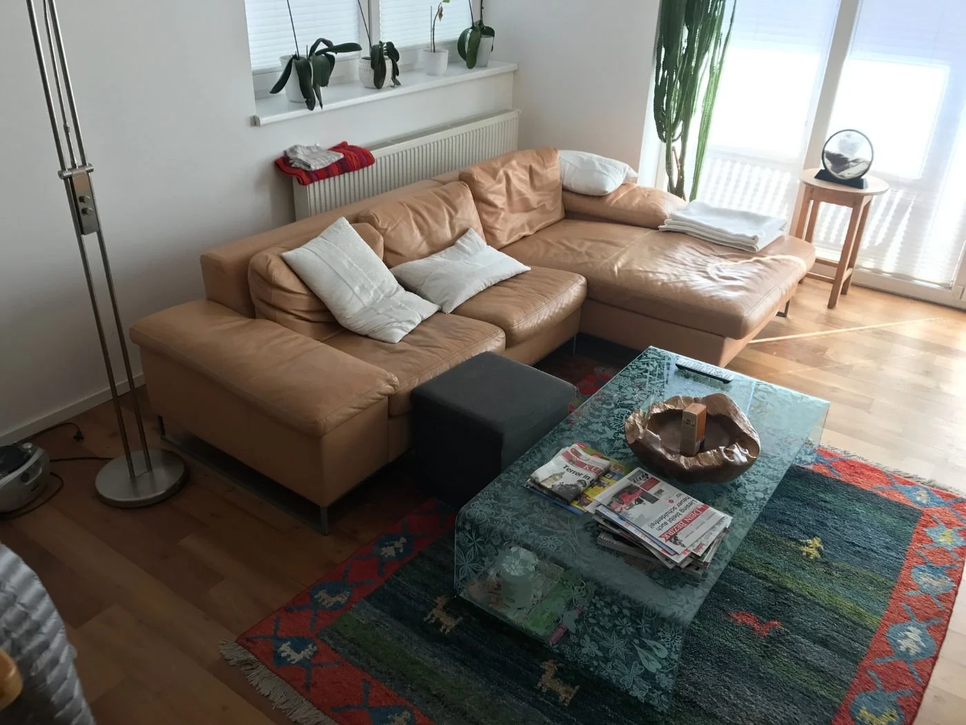 Vorher-Bild eines Wohnzimmers im Altbestand mit Ledersofa, Couchtisch, Teppich und Holzboden als Ausgangssituation vor der Umgestaltung