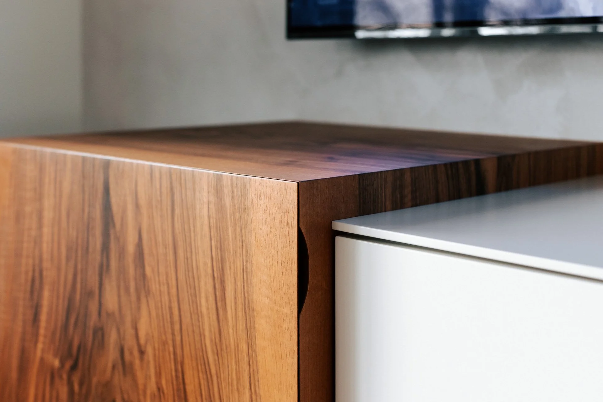 Detail eines maßgefertigten Möbelstücks mit warm gemaserter Holzfront und weißem Schrankelement.