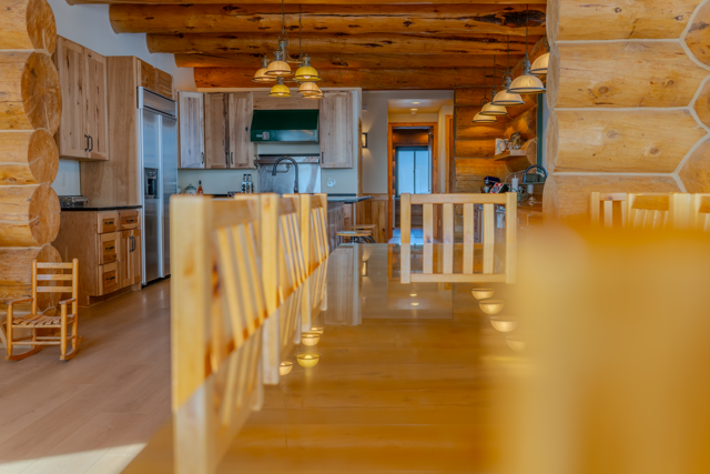 Interior view of a Spokane area rustic kitchen with wooden cabinets, a dining table, and wooden chairs, featuring a vaulted ceiling with exposed beams and hanging lights.