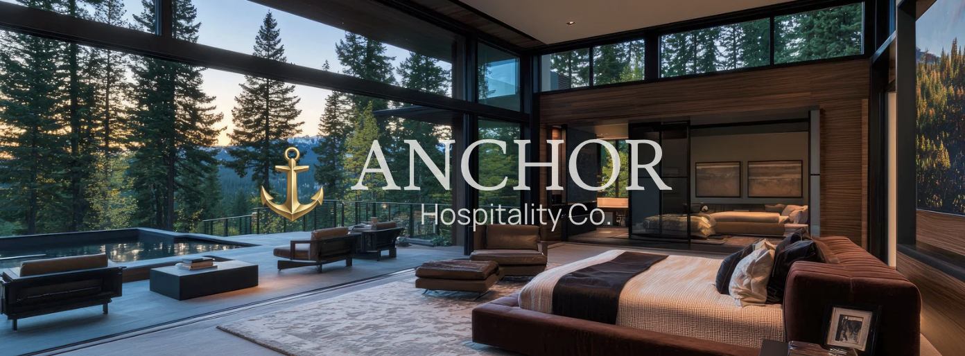 Modern bedroom with large windows overlooking a forest landscape, featuring a bed with pillows, a sitting area with chairs and tables, and a balcony with seating.