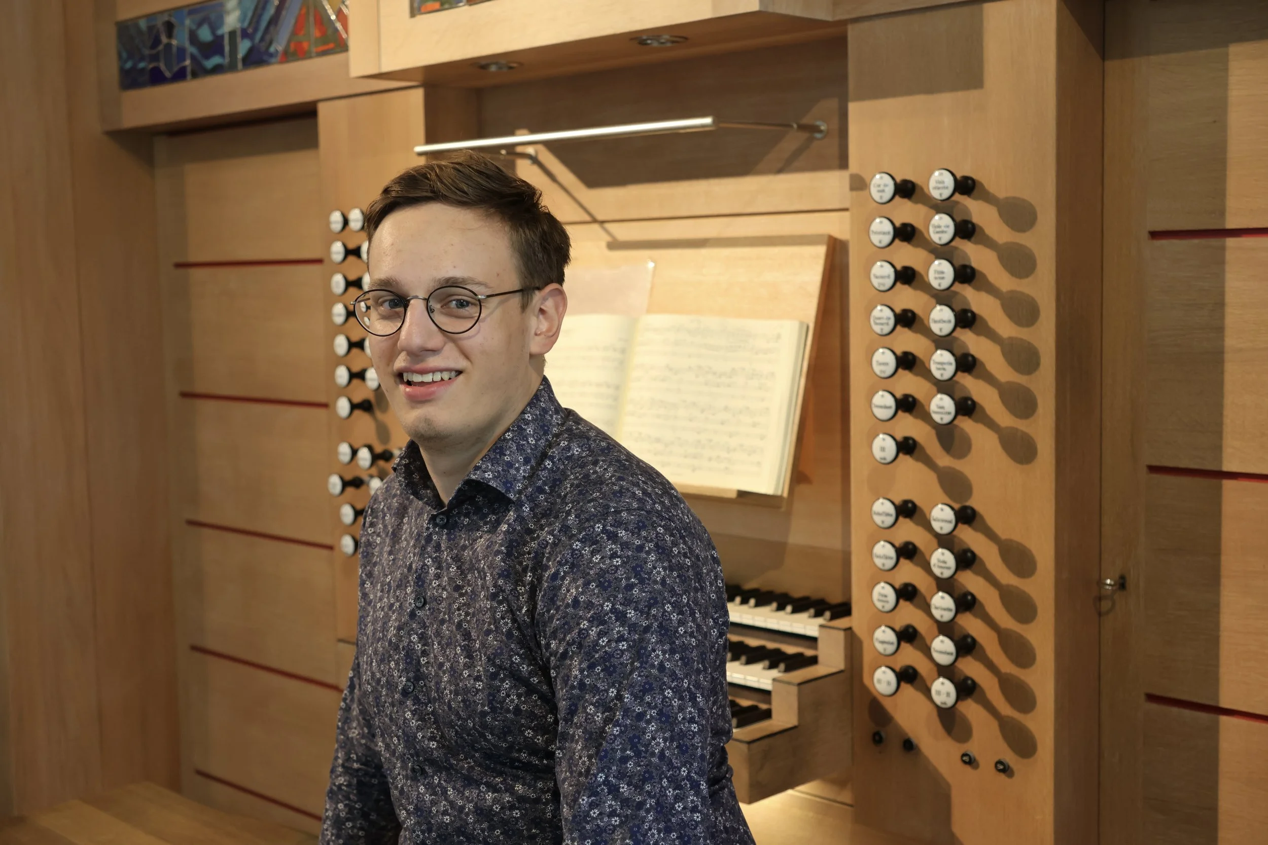 Junger Mann mit Brille und dunklem, gemustertem Hemd vor einer Orgel
