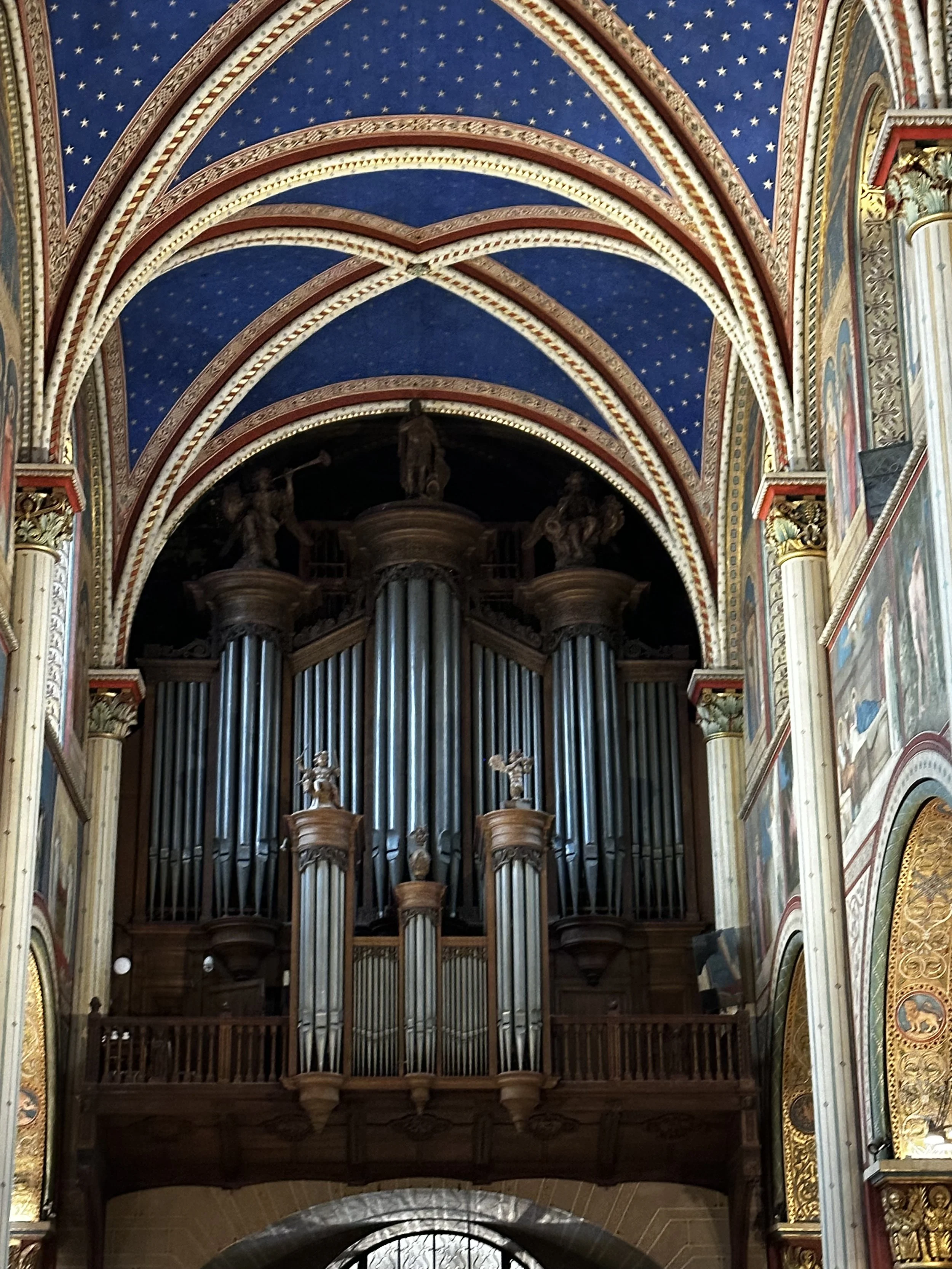 Ein barockartiges Kirchengelände mit einer großen Orgel aus Holz und Metall, umgeben von kunstvoll verzierten Wandmalereien und gewölbten Decken mit Sternenmustern.