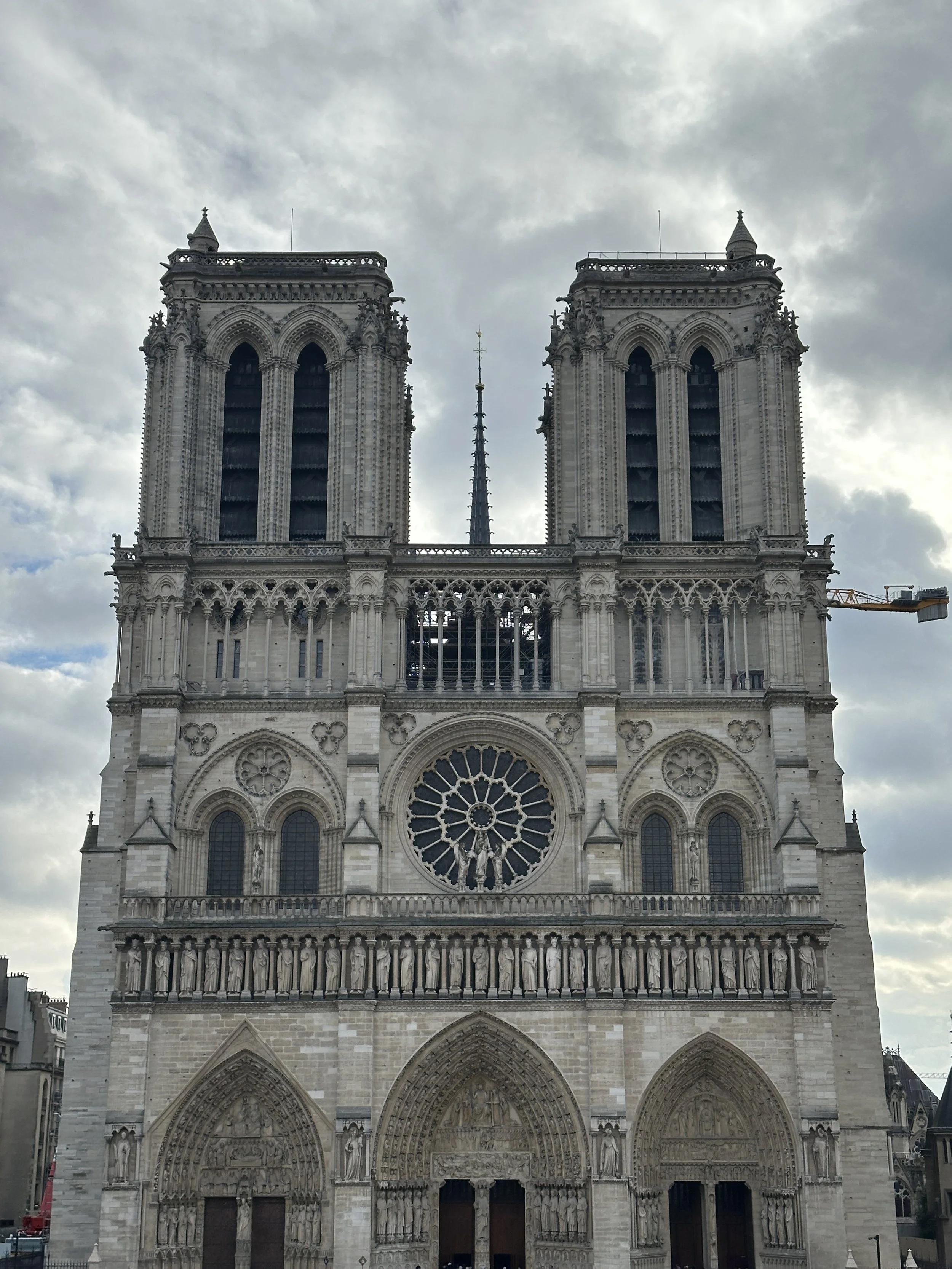 Die Notre-Dame-Kathedrale in Paris mit gotischer Architektur, großen Türmen, Rosettenfenstern und detaillierten Steinmetzarbeiten, bei bewölktem Himmel.