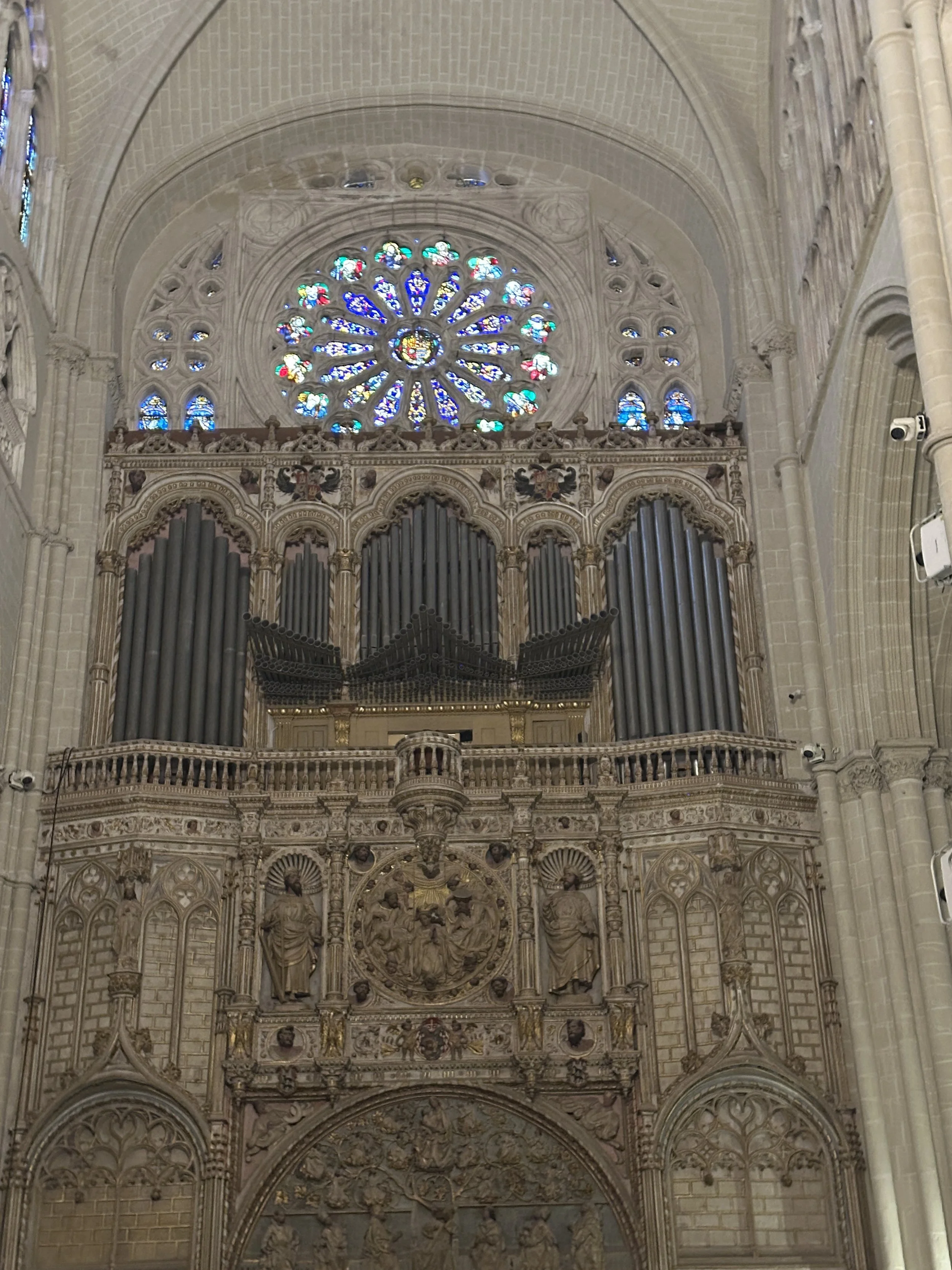 Innenraum einer gotischen Kathedrale mit einem großen bunten rosafarbenen Fenster und einer aufwändig verzierten Orgel mit goldenen Details sowie Skulpturen und steinernen Verzierungen.