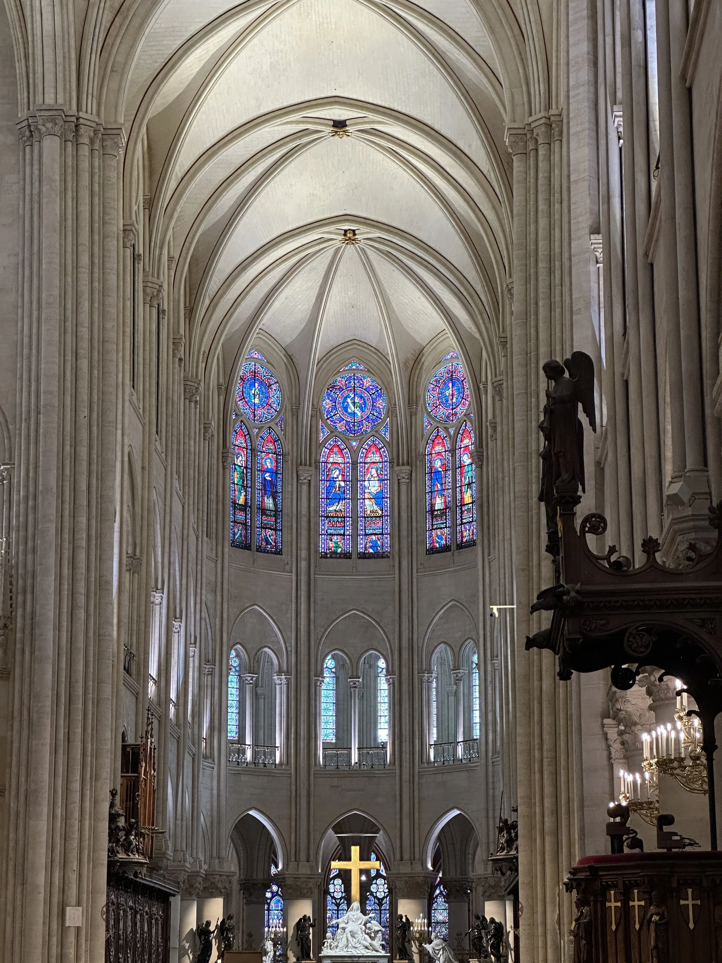 Innenansicht einer prächtigen gotischen Kathedrale mit hohen, gewölbten Decken, bunten Glasfenstern und einer goldenen Kreuz im Altarbereich.
