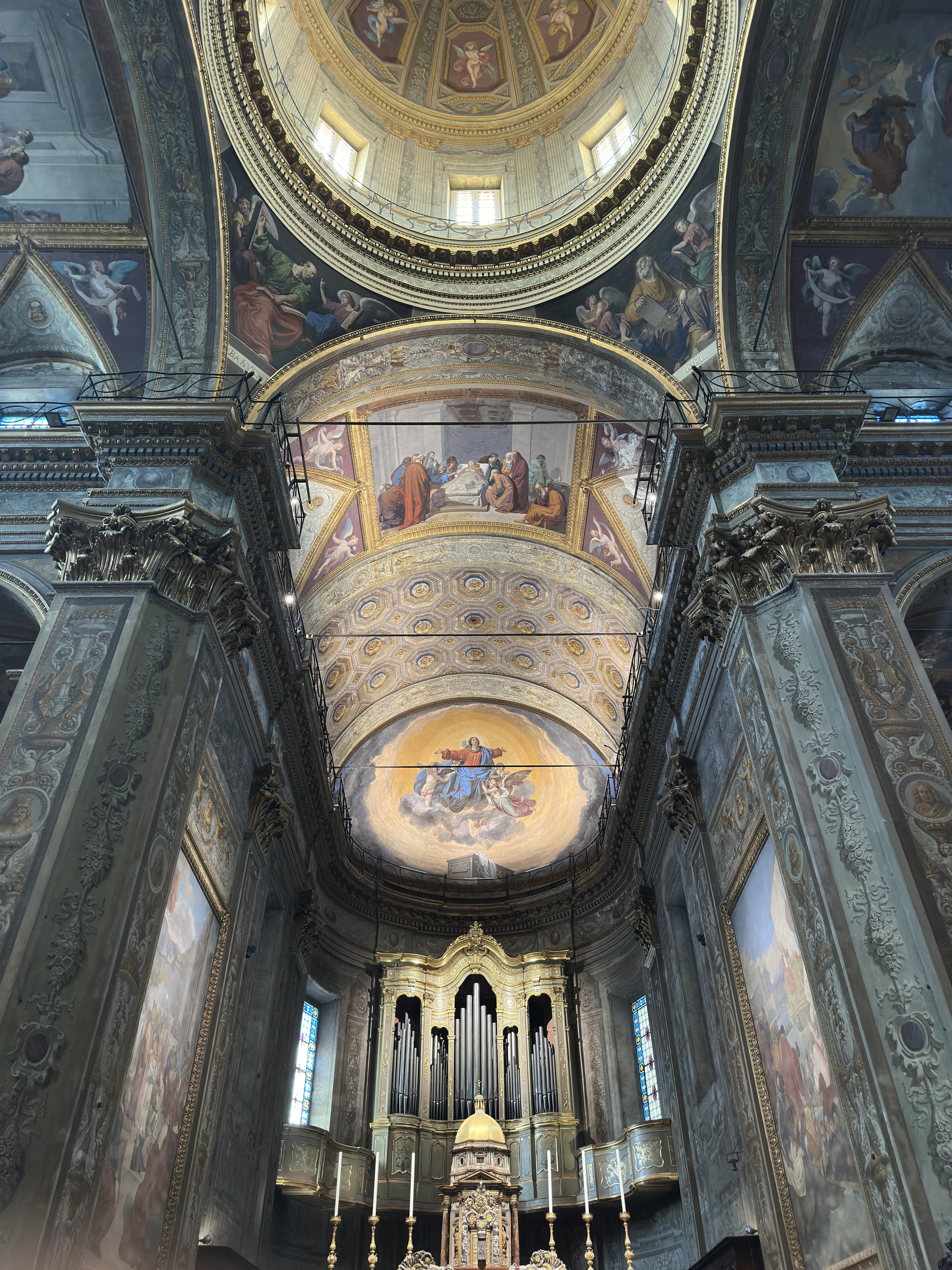 Innenansicht einer barocken Kirche mit aufwendigen Verzierungen, goldenen Akzenten, bemalten Decken und einem großen Orgel im Hintergrund.