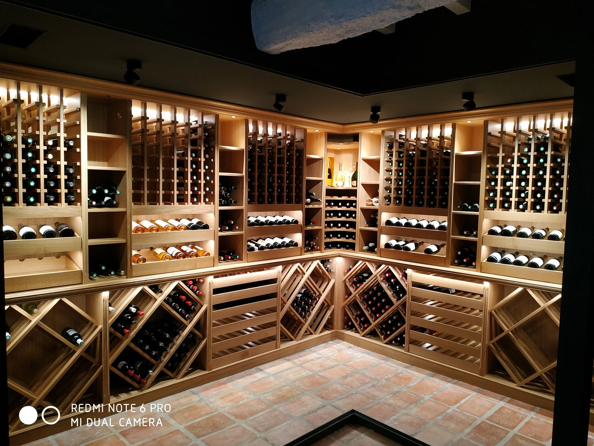 Cave à vins en bois avec étagères contenant de nombreuses bouteilles de vin illuminées par un éclairage doux.