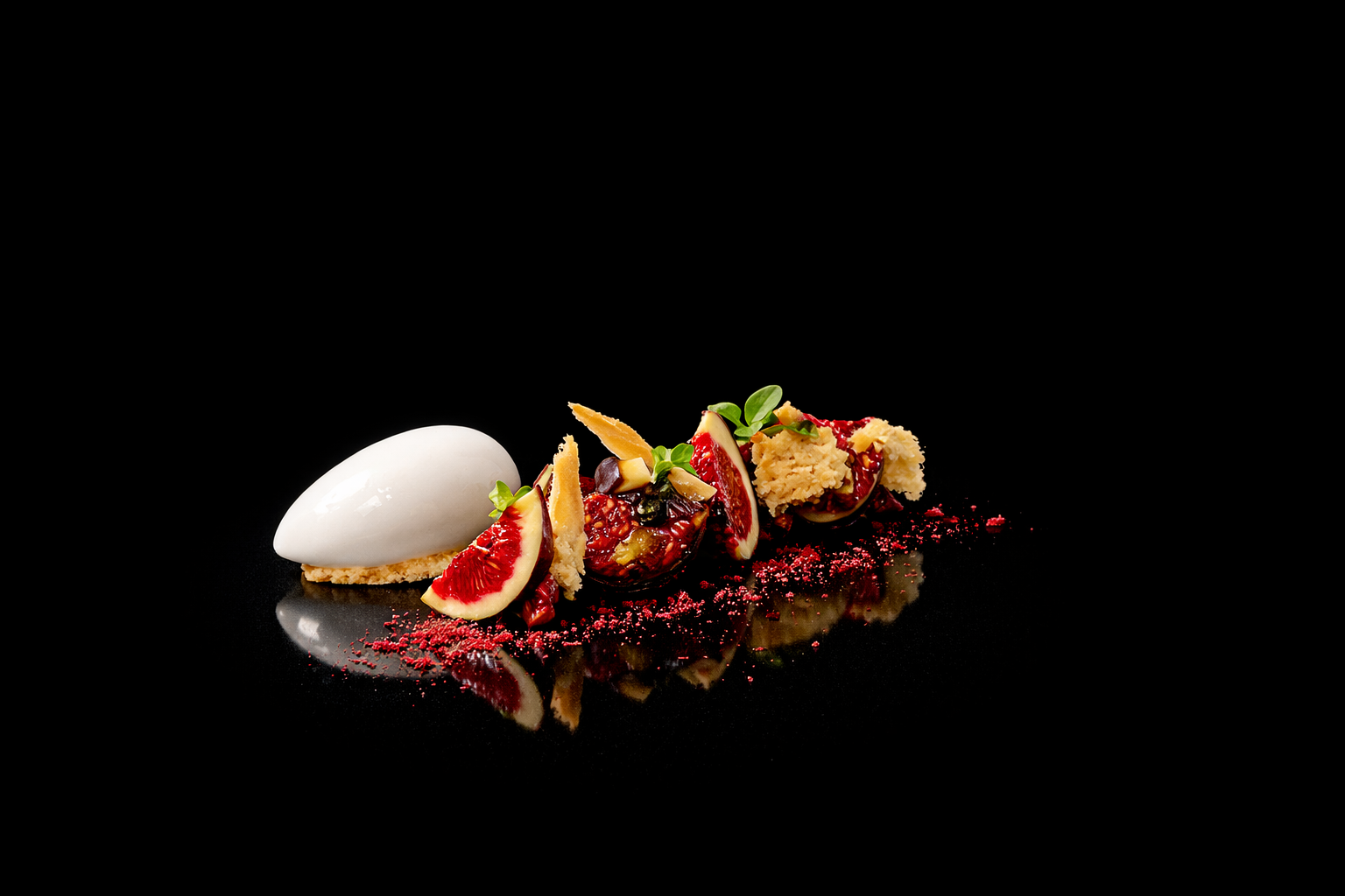 Dessert sophistiqué avec une mousse blanche, morceaux de figues, éclats de biscuit, graines, et micro-pousses, présenté sur un fond noir.