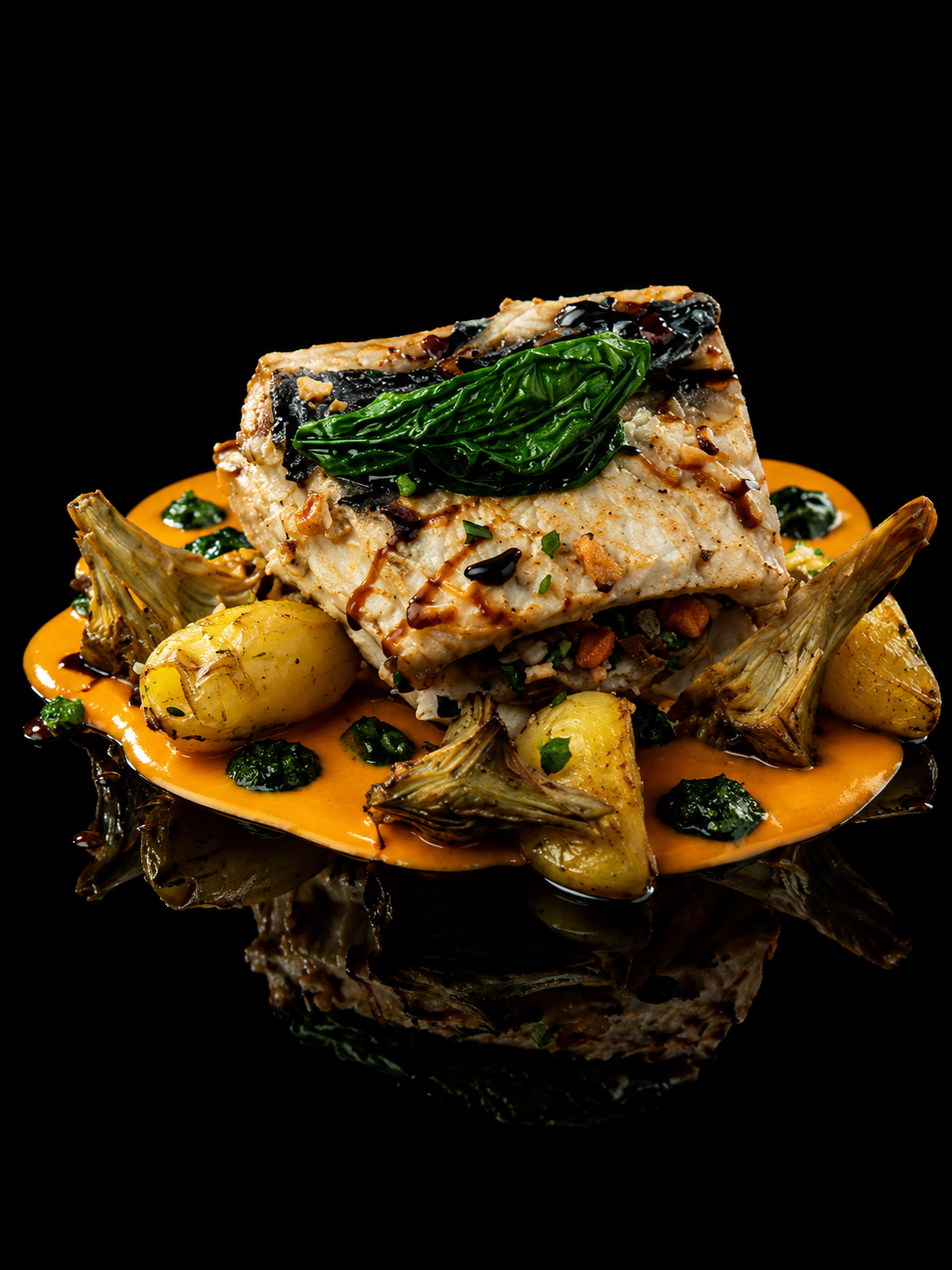 Assiette de poisson blanc avec légumes, sauce-orange et garnitures vertes, présentée sur fond noir.