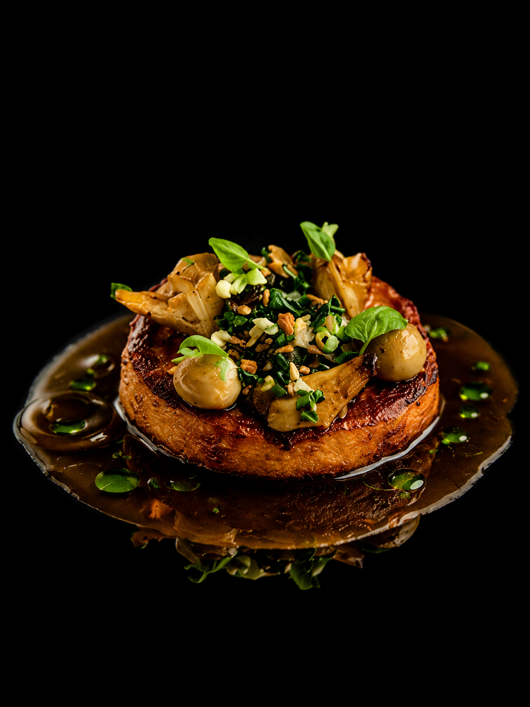Gourmet seared meat steak garnished with sautéed mushrooms, leafy greens, and drizzled with brown sauce on a black background.