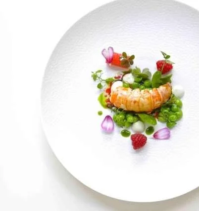 Assiette blanche avec une crevette, des fraises, des mûres, des petits pois et des pétales de fleurs pour la garniture, présentation artistique.