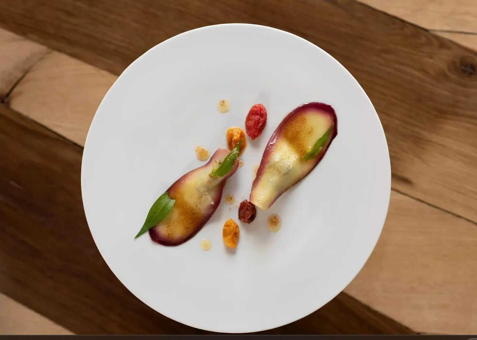 Assiette blanche avec deux poires coupées, garnies de mousse et de feuilles vertes. Autour, des petits morceaux de fruits ou de croustillant, et quelques gouttes de sauce ou de gelée.