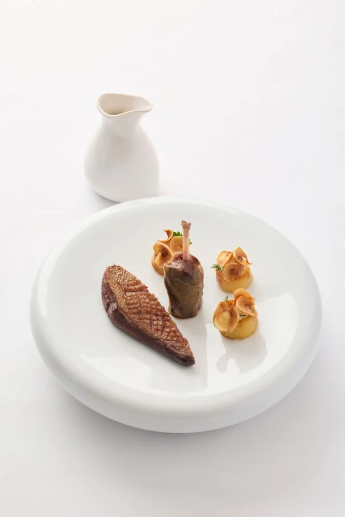 assiette avec un morceau de viande, un petit rôti d'agneau et trois pommes de terre farcies, accompagnée d'une petite cruche blanche