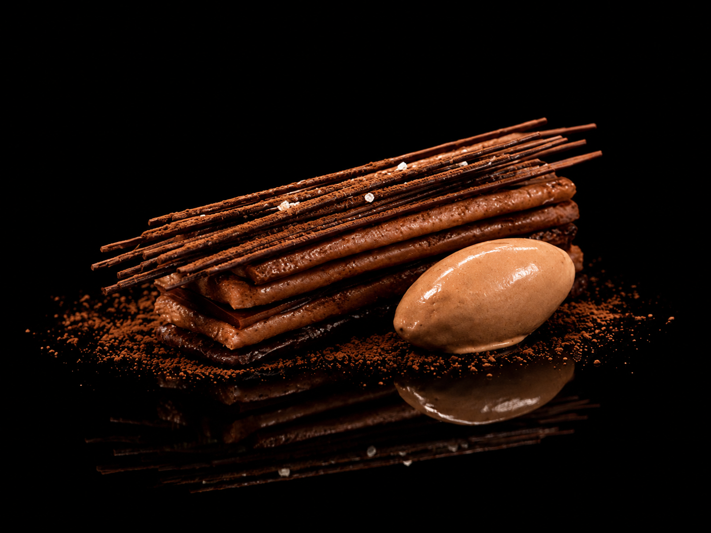 Dessert au chocolat avec des Спиральные палочки en haut et une boule de glace à côté, sur une surface noire.