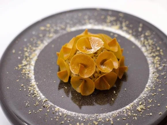 Pâtes farfalles avec une sauce au citron sur une assiette noire, décoration de zeste de citron autour.