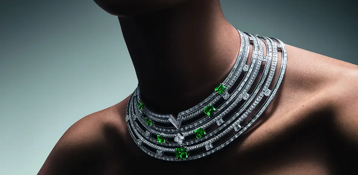 Collier de bijoux en or blanc orné de diamants et de pierres vertes, porté par une personne nue.