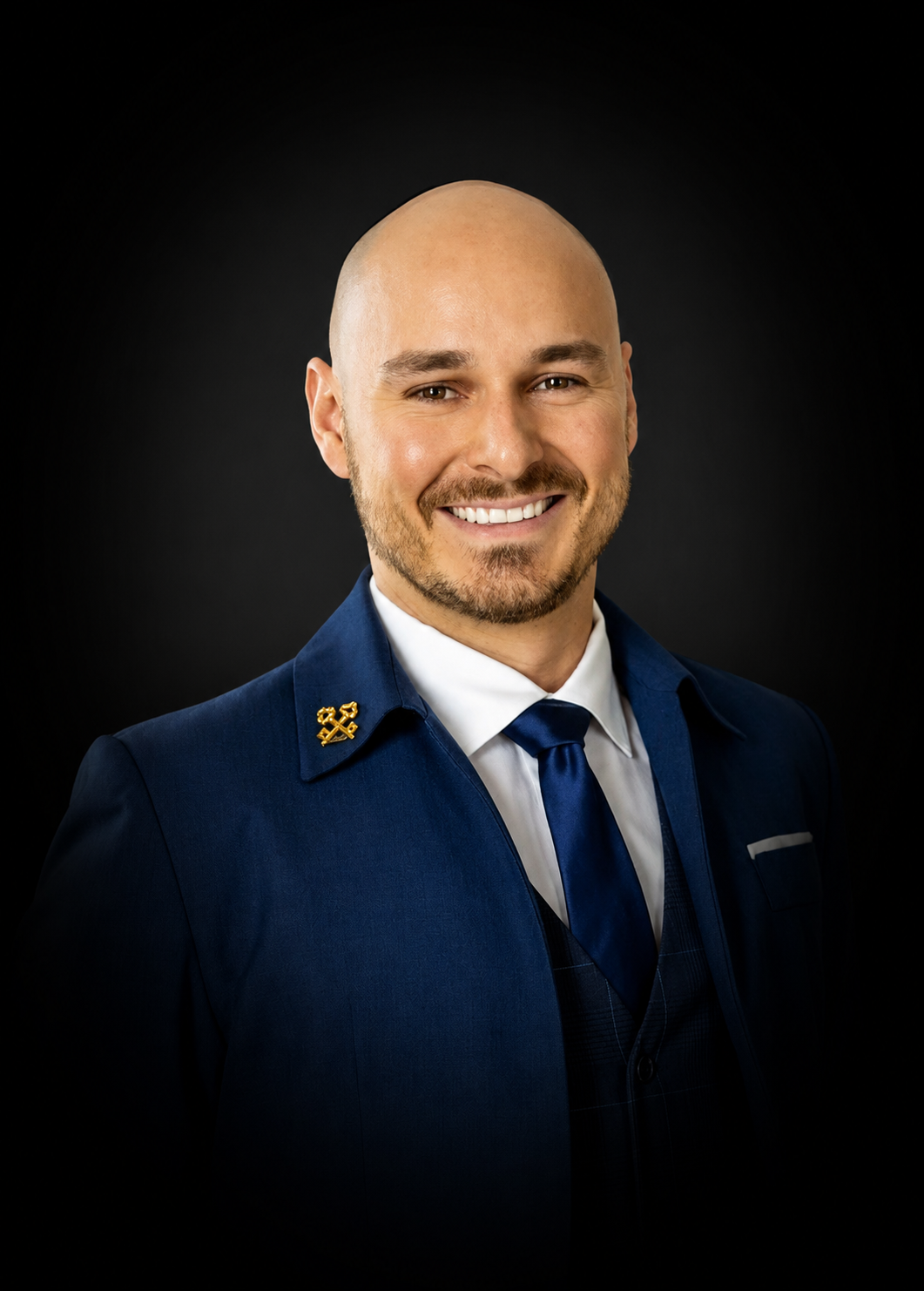 Portrait d'un homme souriant portant un uniforme bleu avec une épingle sur le col, fond noir.