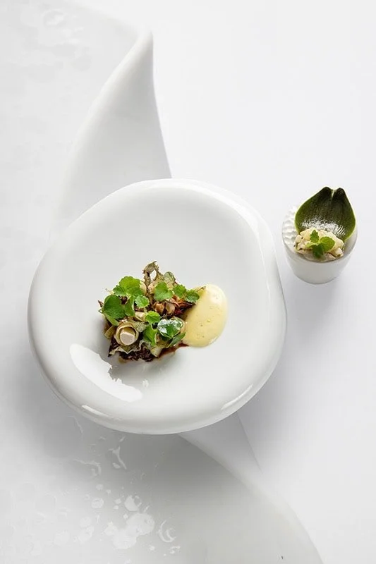 Une assiette gastronomique avec une garniture de légumes verts et une sauce, accompagné d'une petite coupelle avec une crème et un œuf de caille.