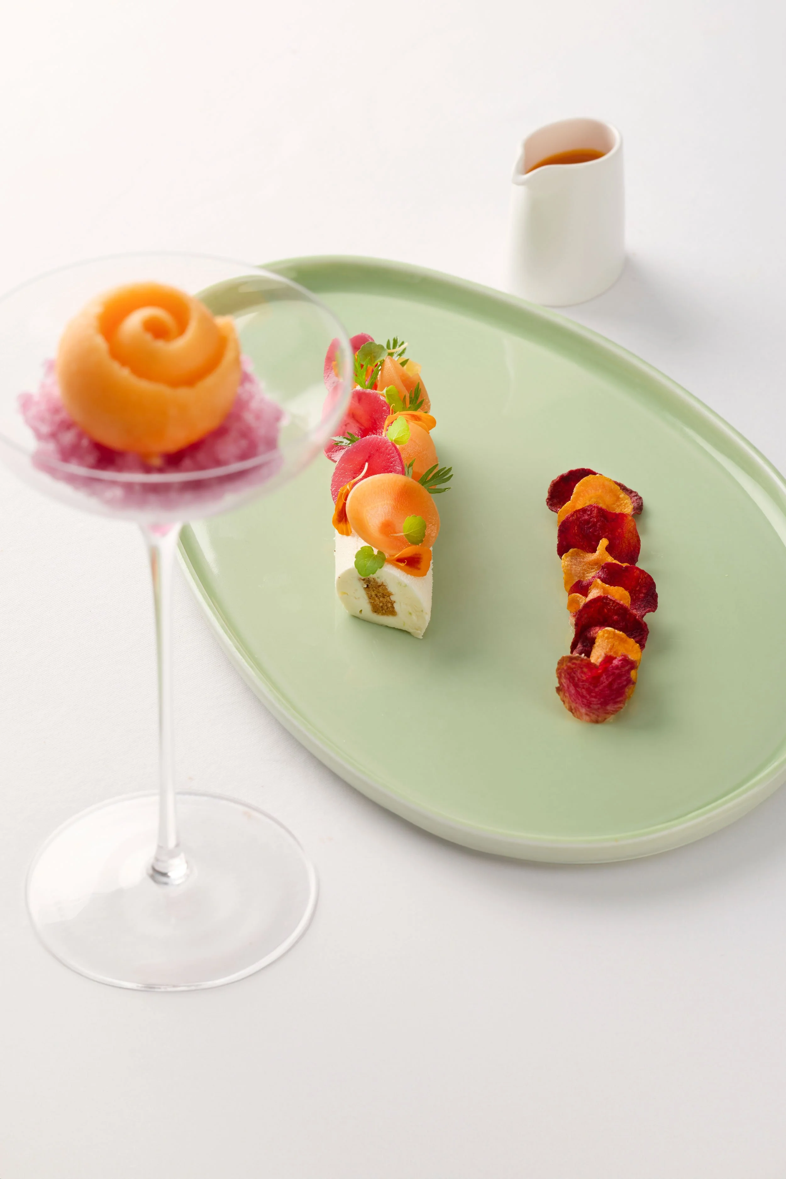 Assortiment de desserts fins avec un sorbet à la vanille et fruits, un gâteau petit four décoré de fruits et une rangée de chips de légumes.