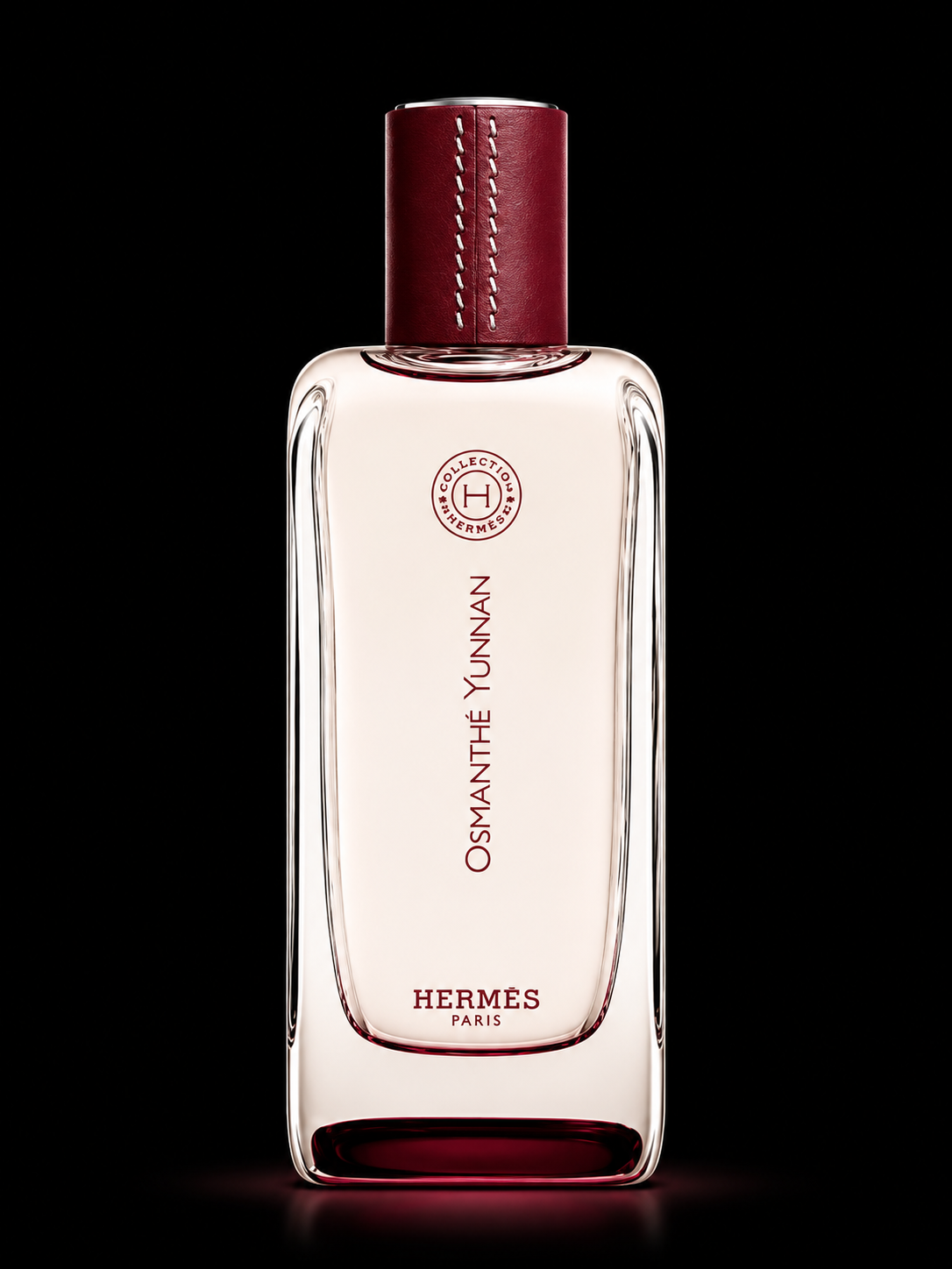 Une bouteille de parfum Hermès Osmanthé Yunnan avec un capuchon en cuir rouge foncé et un fond noir.