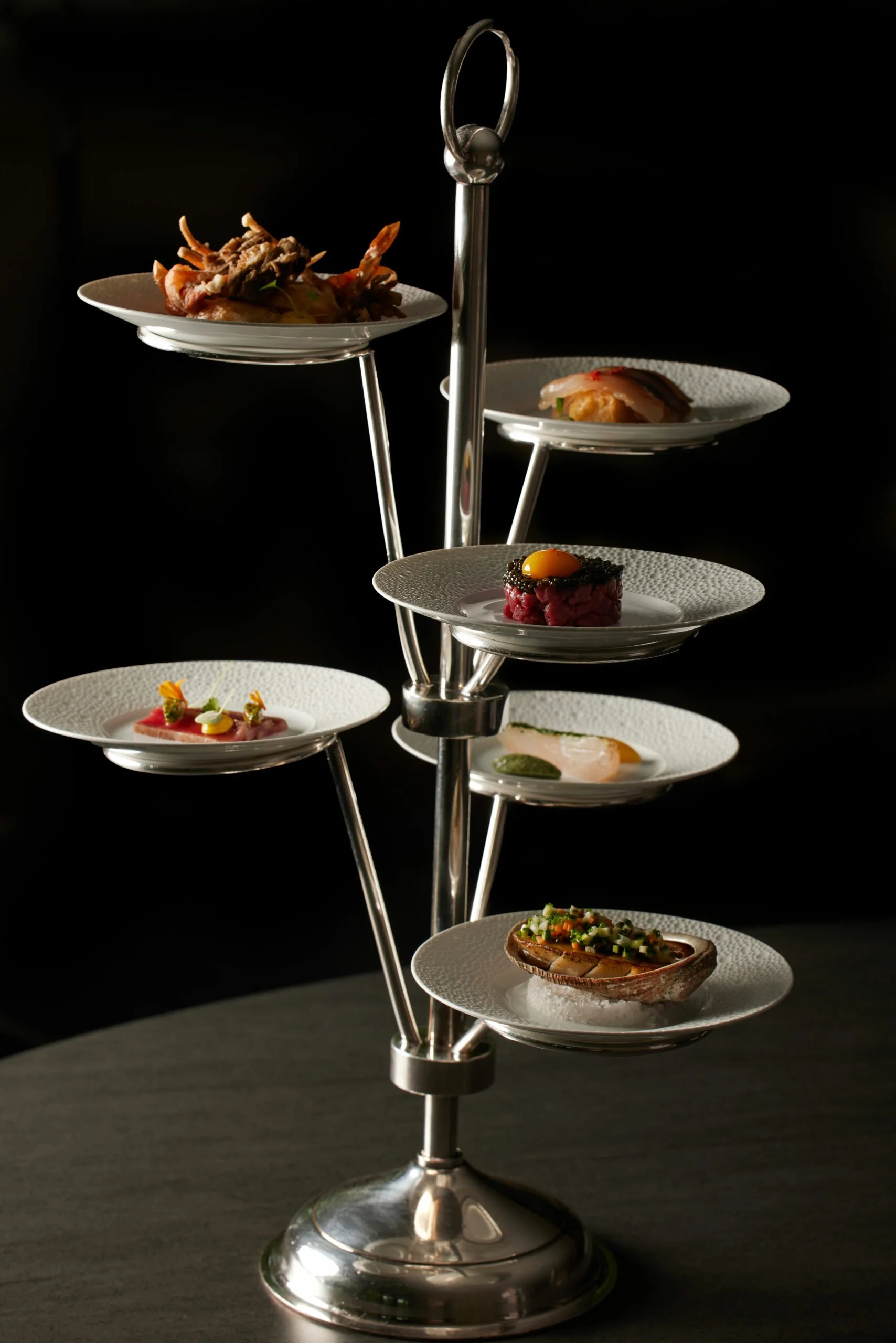 Un présentoir en métal avec plusieurs petites assiettes contenant des amuse-gueules et des plats sophistiqués, présentés en haute cuisine.