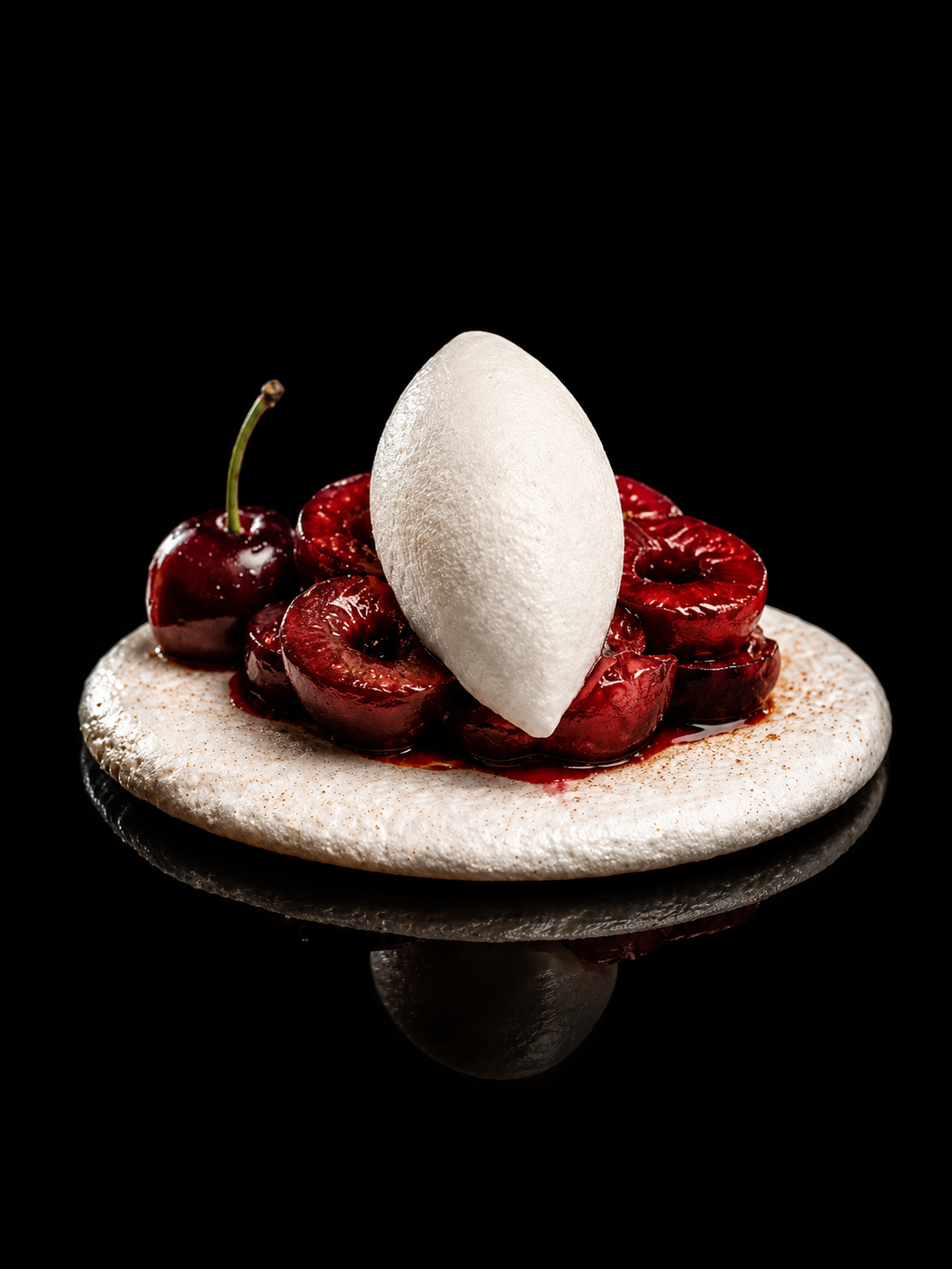 Tartelettes aux cerises avec une meringue et une quenelle de crème, sur un fond noir.