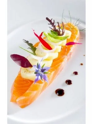 Tartare de saumon décoré de légumes et de fleurs comestibles sur une assiette blanche.