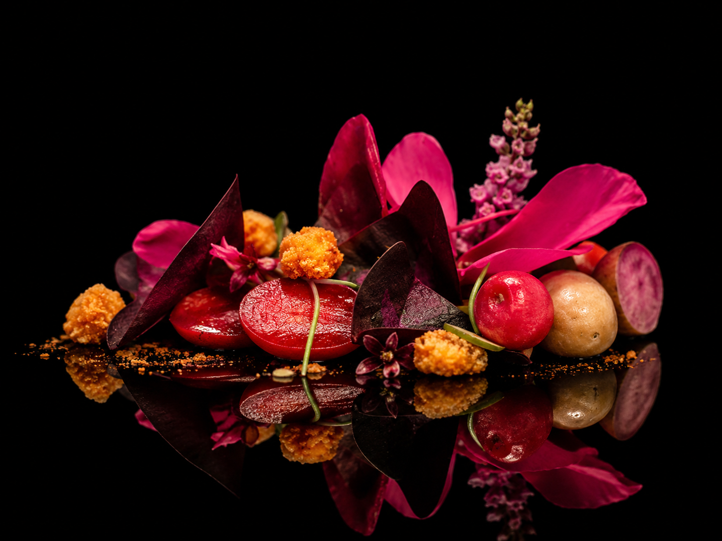 Un arrangement floral artistique avec des fleurs roses, rouges, et des éléments végétaux, reflet sur une surface noire.