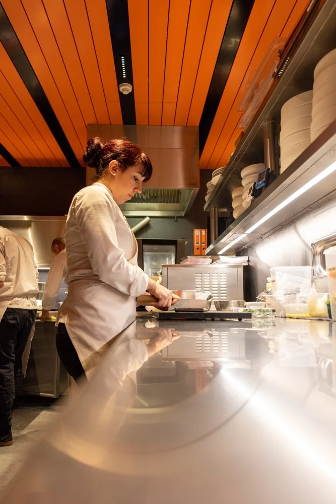 Une femme en uniforme de cuisine prépare des aliments dans une cuisine professionnelle moderne.
