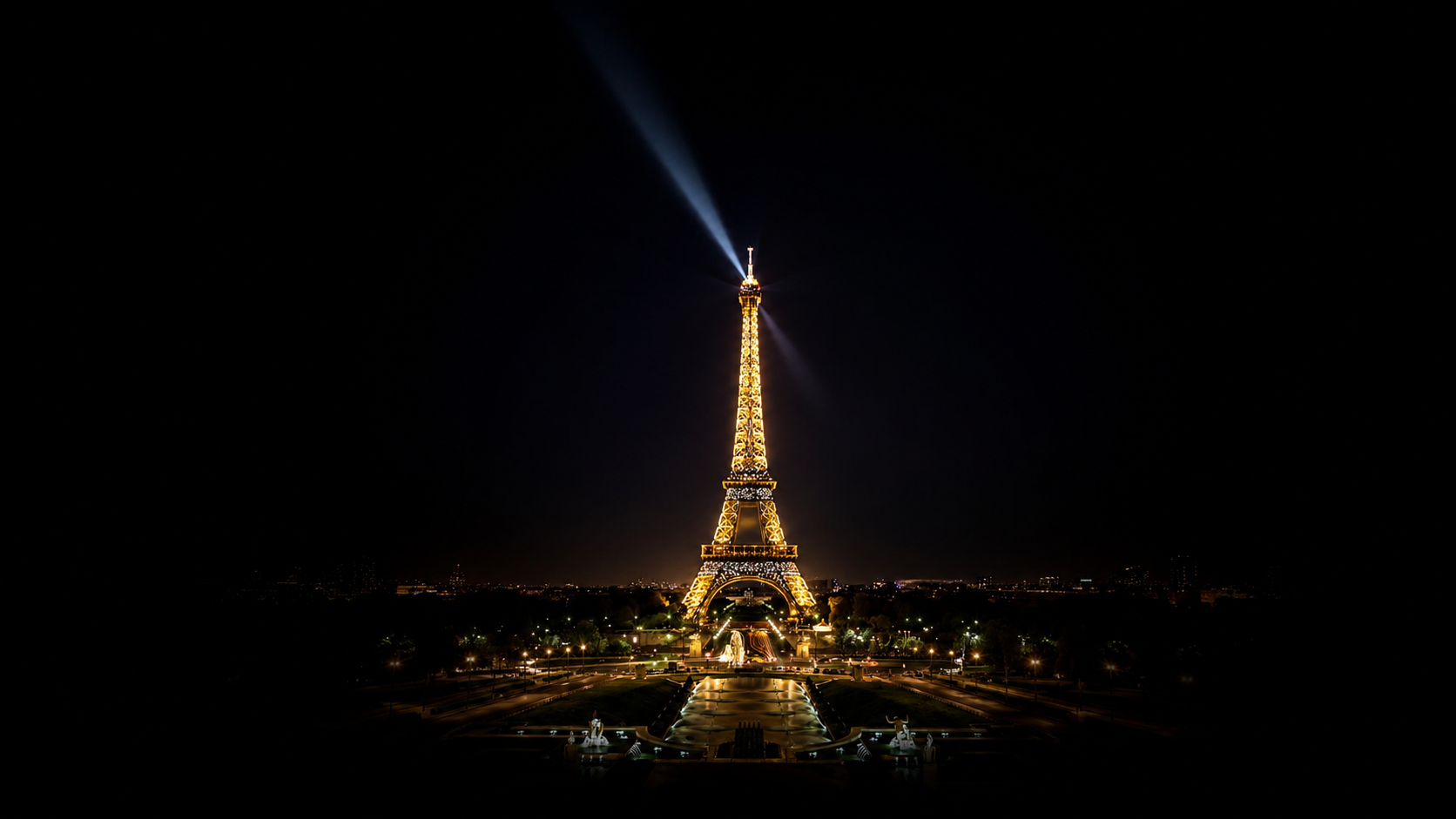 Tour Eiffel illuminée la nuit avec un faisceau lumineux en haut, reflet des lumières de la ville en dessous, dans un ciel noir.