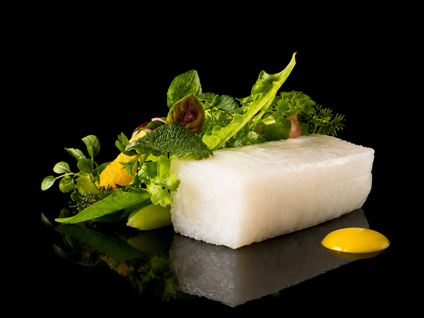 Une pièce de fromage blanc avec des feuilles de salade, des herbes, des morceaux d'orange et une goutte de sauce jaune sur un fond noir