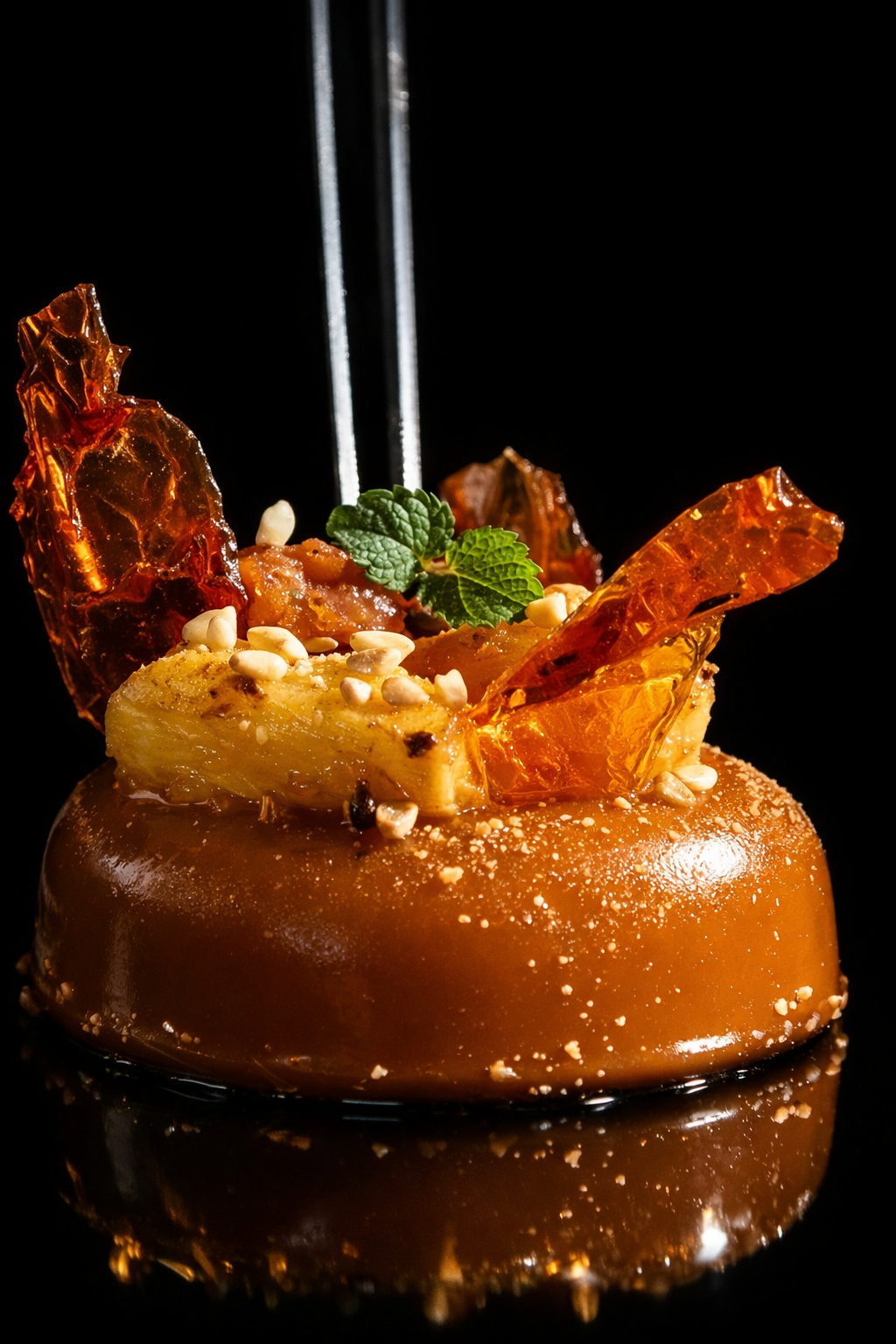 Gâteau décoré avec caramel, noix, menthe et morceaux de fruits, présenté sur un fond noir.
