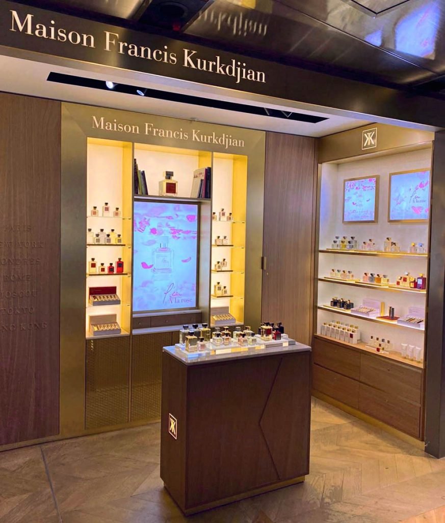 Vitrine d'une boutique de parfums Maison Francis Kurkdjian avec différentes bouteilles exposées et écrans d'affichage