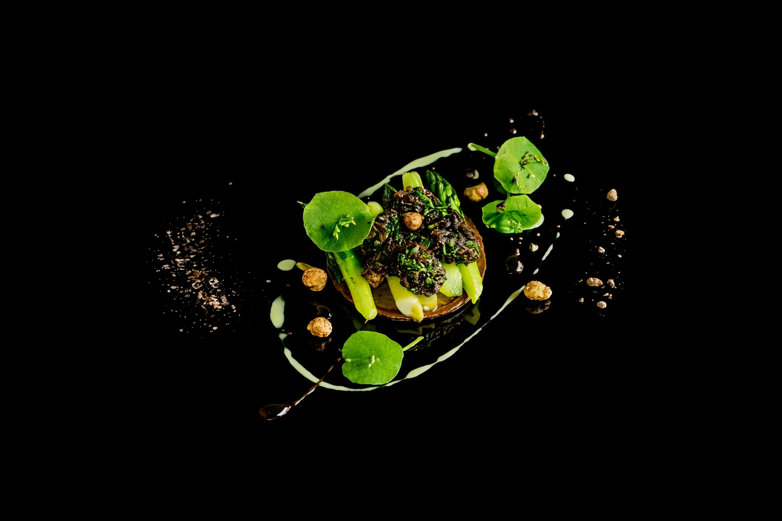 Assiette de présentation culinaire avec des légumes verts, sauce et garnitures, décorée avec des petits éléments et disposée sur un fond noir