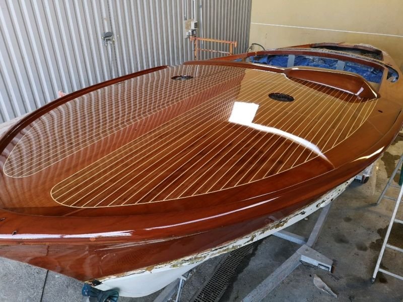 Un bateau en bois en cours de restauration dans un atelier, avec un intérieur en bois verni et des structures en carbone.