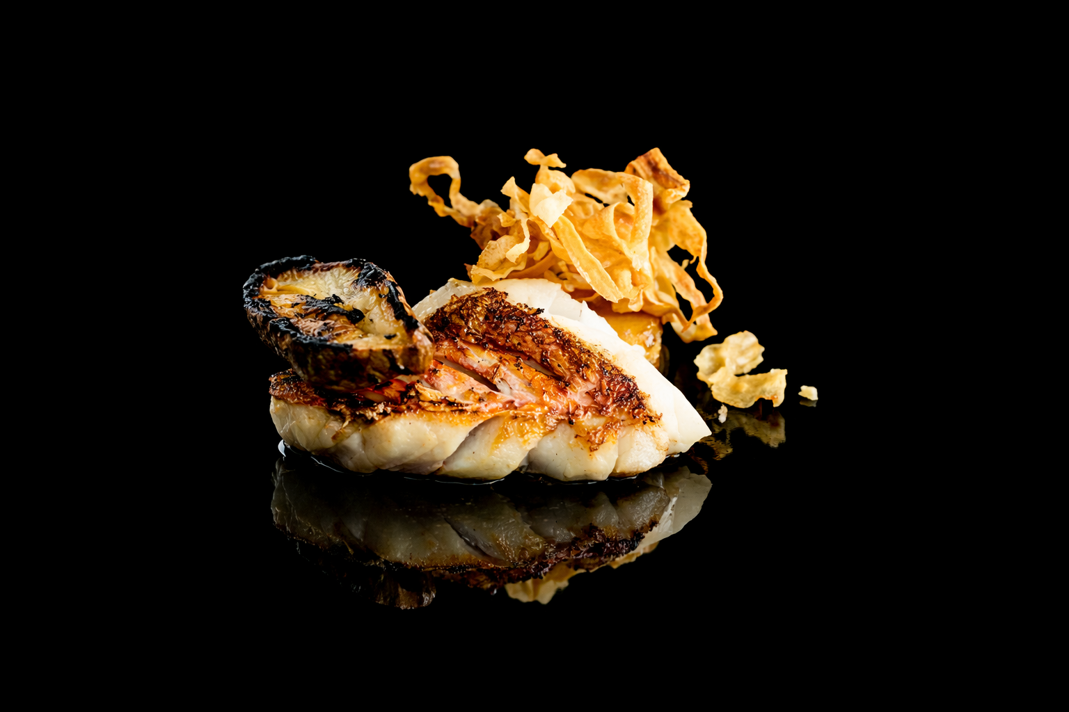 Filet de poisson grillé avec une tranche de citron grillé et des chips croustillantes, présenté sur fond noir.