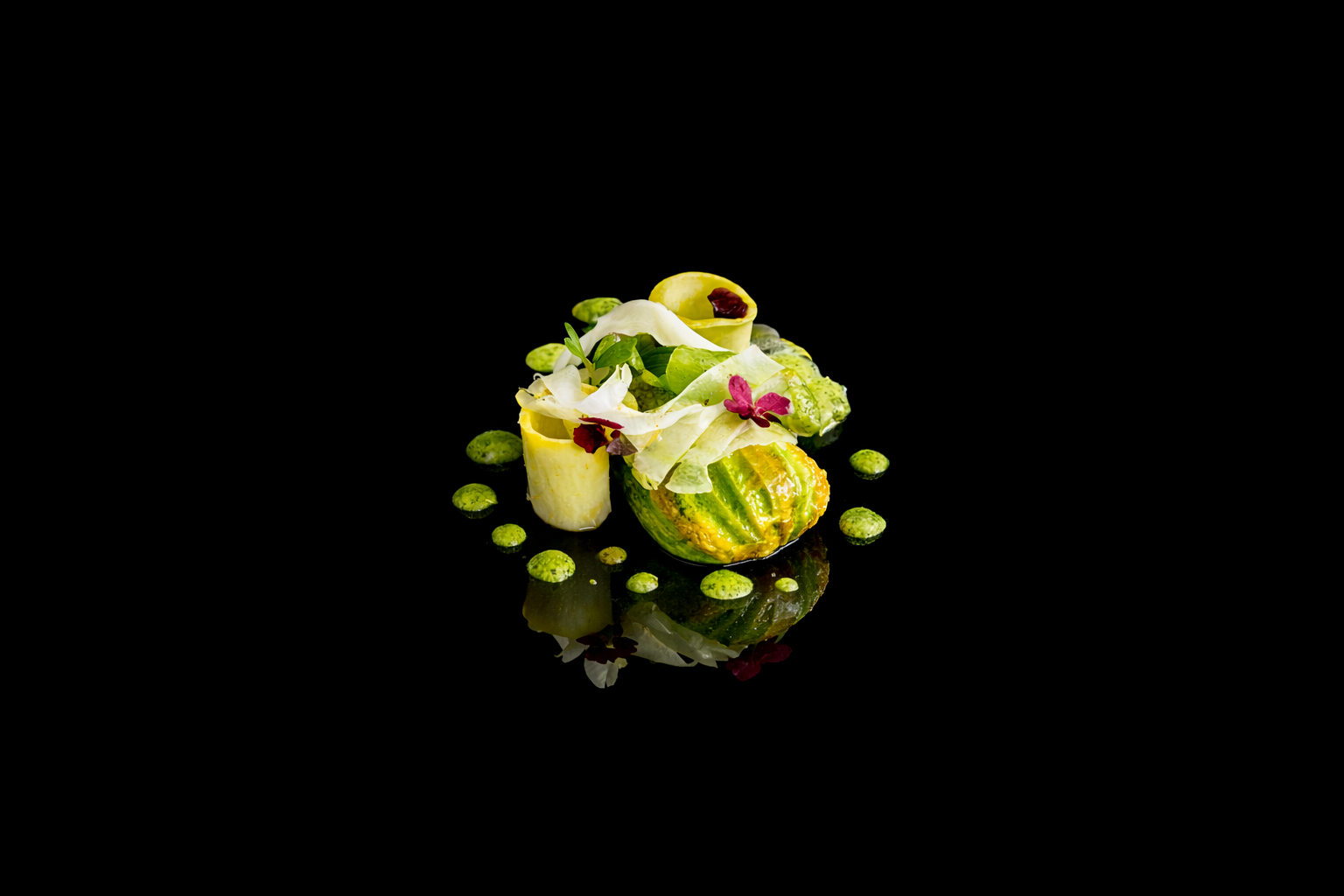 Assiette de présentation de légumes et fleurs comestibles, avec une garniture artistique sur un fond noir.