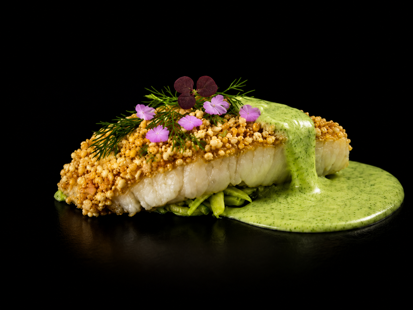 Poisson blanc en croûte de graines, nappé d'une sauce vert clair, décoré de petites fleurs violettes, de feuilles d'herbes et de pousses végétales, présenté sur fond noir.