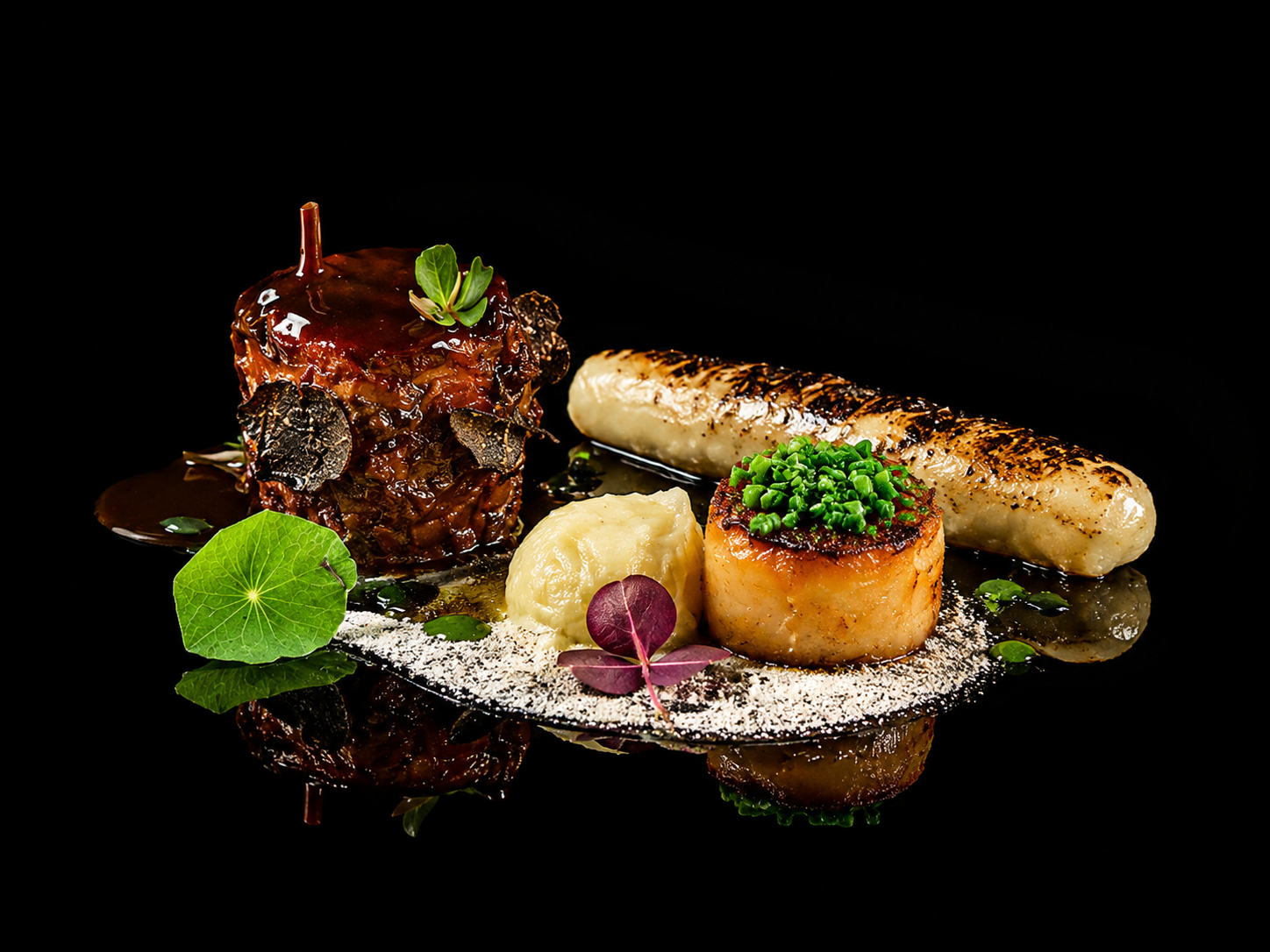 Assiette gastronomique avec un rôti en sauce, purée, fruits de mer, garnitures, et décorations végétales sur fond noir.