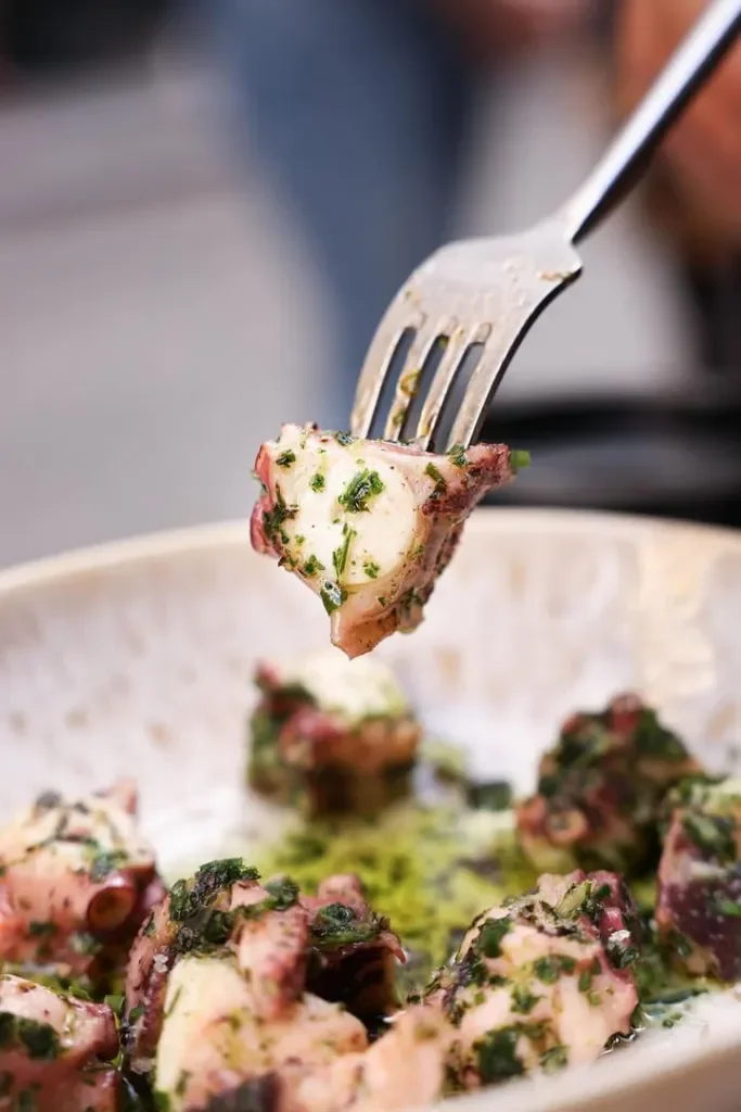 Cubes de poulpe avec une sauce verte dans un bol, une fourchette piquant une pièce de poulpe
