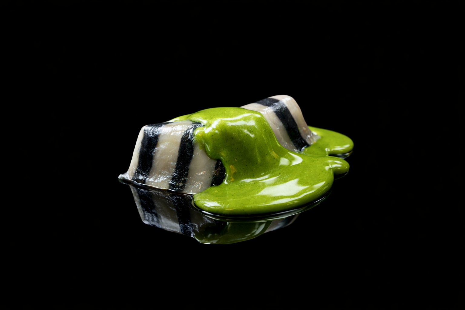 Gâteau en forme de rouleau avec un glaçage noir et blanc, recouvert d'une sauce verte brillante, posé sur un fond noir.