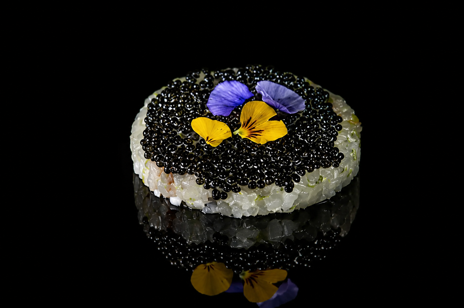 Tartare de sushi décoré de fleurs violettes et jaunes, sur un fond noir