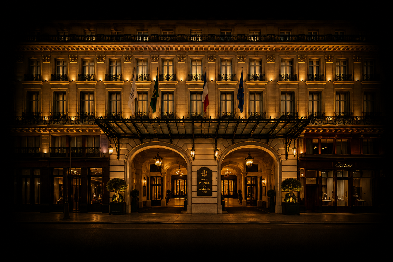 Façade illuminée de l'hôtel Prince de Galles à Paris la nuit, avec des drapeaux français, européen et autres devant l'entrée.