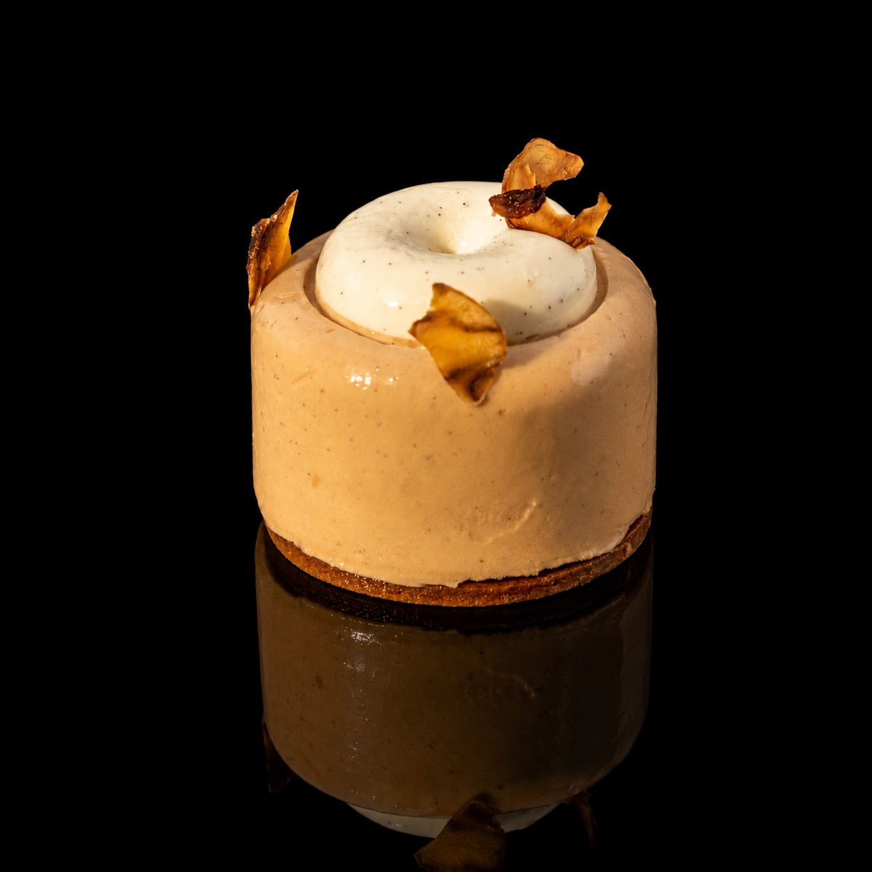 Un gâteau rond avec une décoration de crème blanche et des morceaux de ce qui semble être de la noix ou du caramel sur le dessus, présenté sur un fond noir.