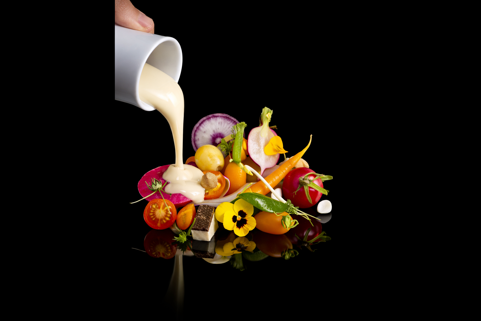 Une soupe de légumes colorés avec du lait crème étant versé dessus, sur fond noir.