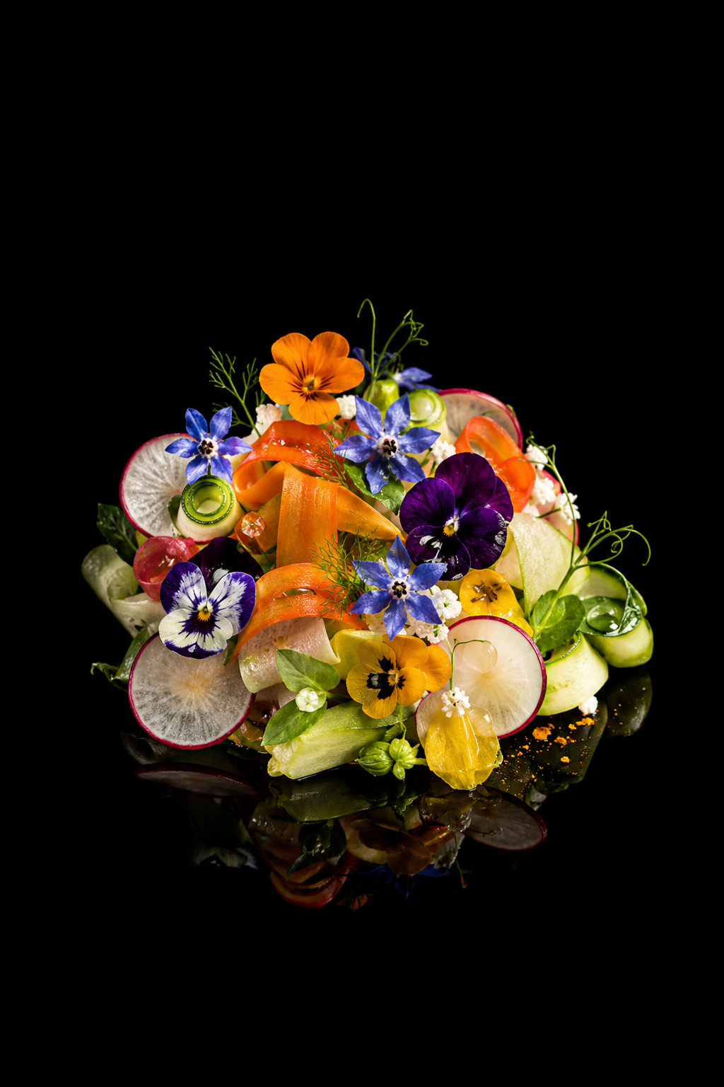 Salade colorée composée de radis, concombre, carottes, fleurs comestibles et herbes, sur fond noir.