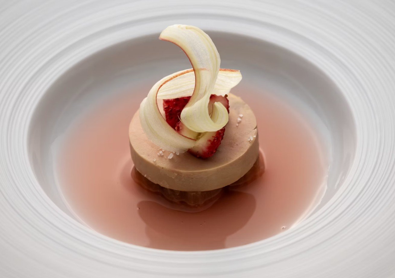 Dessert avec une base de mousse ou crème, garnie de morceaux de fraise et décorée de spirales de zeste de citron, servi dans une assiette blanche.